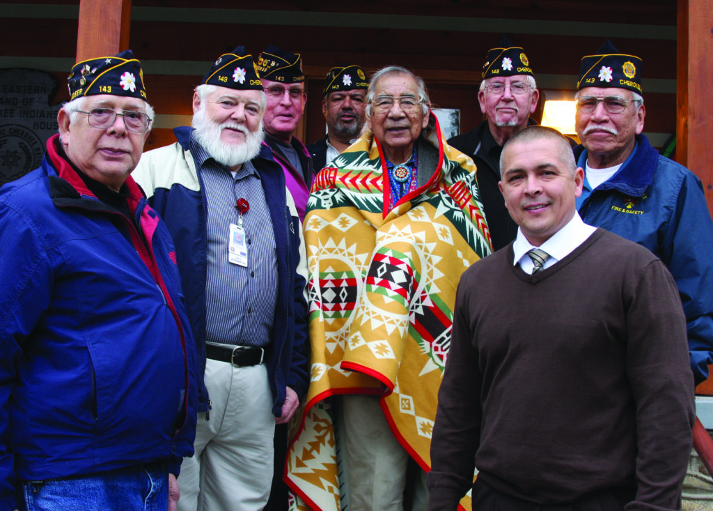 Jerry Wolfe (center in blanket), an EBCI tribal elder from the Yellowhill Community, was honored in Tribal Council on Thursday, Feb. 14.  Wolfe was honored as a World War II veteran and Cherokee traditionalist at the USET Impact Meeting held in Washington earlier this month.  He was unable to attend the event, and several Tribal Council representatives accepted a Pendleton blanket on his behalf.  Wolfe was presented with that blanket on Thursday.  He is shown here on Thursday with members of the Steve Youngdeer American Legion Post 143 and Principal Chief Michell Hicks (front row right).  (LYNNE HARLAN/EBCI Public Relations) 