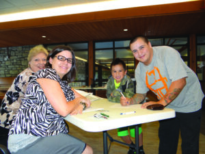 James Maney (right) opens a matched savings account for his son, Champ, during the Kituwah Savings Program kick-off on Thursday, Sept. 26.  They are assisted by First Citizens Bank employees Dinah Smith (left) and Michelle Cochran (2nd from left). (Photo courtesy of Shawn Spruce) 