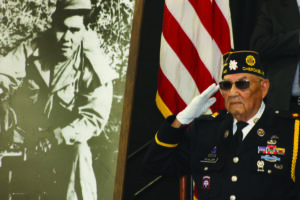 WWII veteran Reuben Taylor salutes during the singing of the National Anthem beside a photo of Pfc. Charles George that was display at Thursday’s event. 