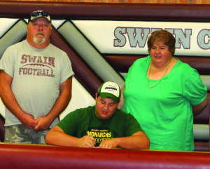 Brent Gunter (seated), whose grandfather, Tim Beck, is an EBCI tribal member, signs a letter of intent on Friday to play college football this fall at Methodist University as his parents Lance and Jilinda Gunter look on.  