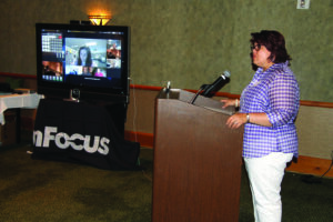 As her remarks are streamed live via a new device known as a Mondopad (left), Chairperson Terri Henry speaks during the opening of the EBCI Technology Expo. 