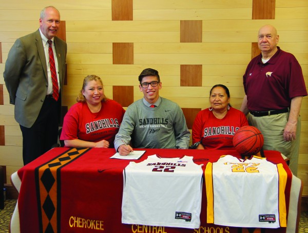 Dustin Johnson (seated center), Braves senior point guard, signs a scholarship on Wednesday, May 27 to play basketball next season for the Sandhills Community College Flyers in Pinehurst.  Shown (left-right) are Mike Apple, Sandhills head basketball coach; Winona Duran Johnson, Dustin’s mother; Johnson; Sally Durant, Dustin’s grandmother; and Willis Tullos, Braves head coach.  (SCOTT MCKIE B.P./One Feather photos)
