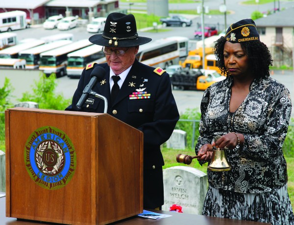 During a Ringing of the Bell of Honor ceremony at a Memorial Day Observance at the Yellowhill Veterans Cemetery on Monday, May 25, Col. Bob Blankenship (Ret.) reads a list of EBCI tribal members who were killed in action as Legionnaire Phyllis Shell rings a bell in their honor and memory.  (SCOTT MCKIE B.P./One Feather photos) 
